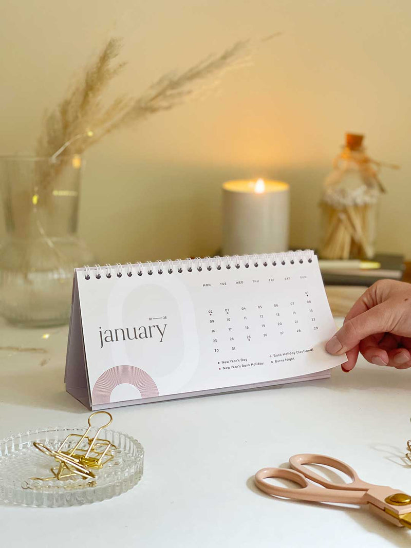 2023 standing desk calendar showing a month view of January 2023 with stationery accessories on a desk