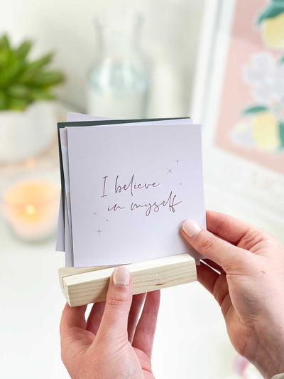 Holding an affirmation card desk with positive quotes reading I believe in myself, to be displayed into a pine wooden holder on a desk