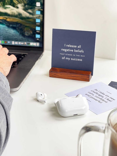 Dark blue quote card in wooden stand with a positive daily affirmation next to man working at his office desk