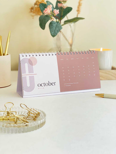 Womens office desk with a standing 2023 desktop calendar displaying a month view of october 2023